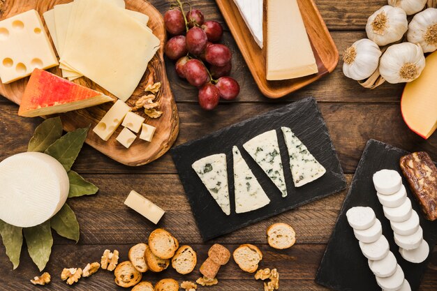 Stück verschiedene Käsesorten mit Trauben; Brotscheibe; Walnuss und Knoblauch auf dem Schreibtisch