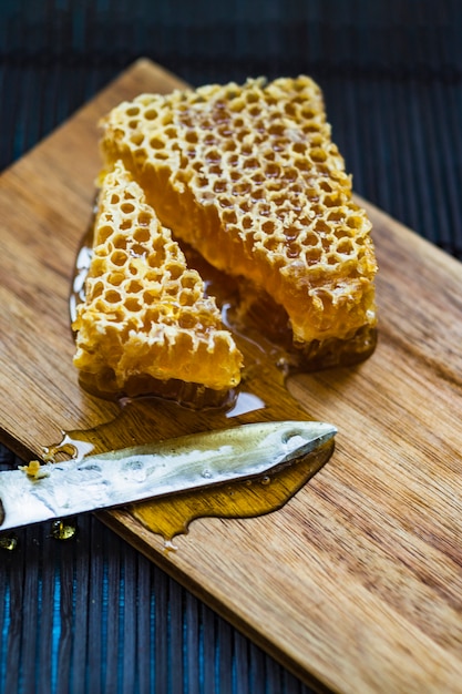 Stücke der Bienenwabe und des Messers auf hölzernem hackendem Brett