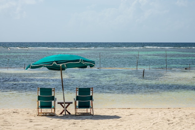 Stühle und ein großer Sonnenschirm am Strand an einem klaren, sonnigen Tag