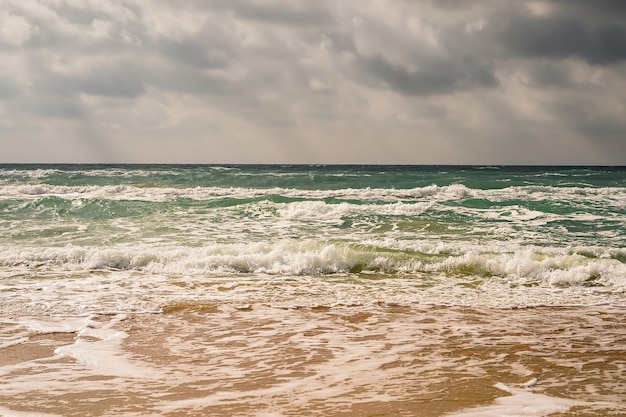 Sturm am Sandstrand der Schwarzmeerküste, smaragdgrünes Wasser, warmer Tag. Die Sonnenstrahlen bahnen sich ihren Weg durch die Wolken am Himmel.