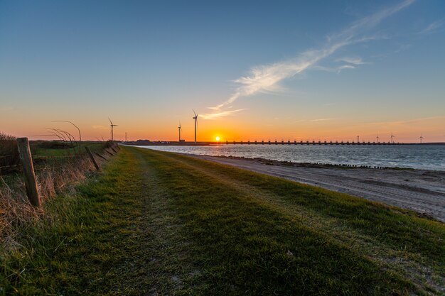 Sturmflutbarriere und Windmühlen in der Provinz Zeeland in den Niederlanden bei Sonnenuntergang