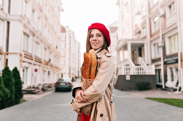 Stylich moderne hübsche Frau, die rote Baskenmütze und beige Graben trägt