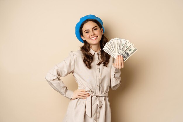 Stylische junge Frau mit Geld in bar, lächelnd und posiert zufrieden beim Einkaufen im Stehen ...