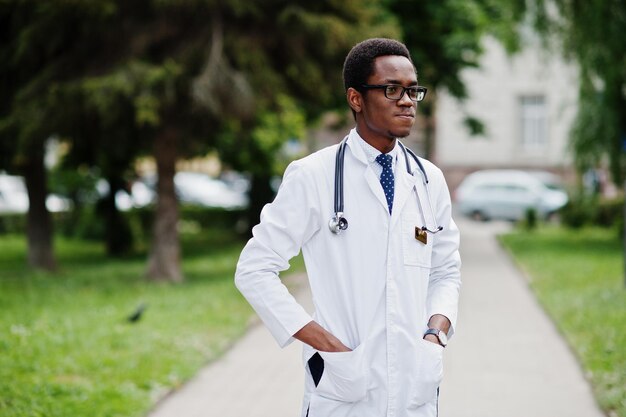 Stylischer afrikanisch-amerikanischer Arzt mit Stethoskop und Laborkittel an Brille im Freien gestellt