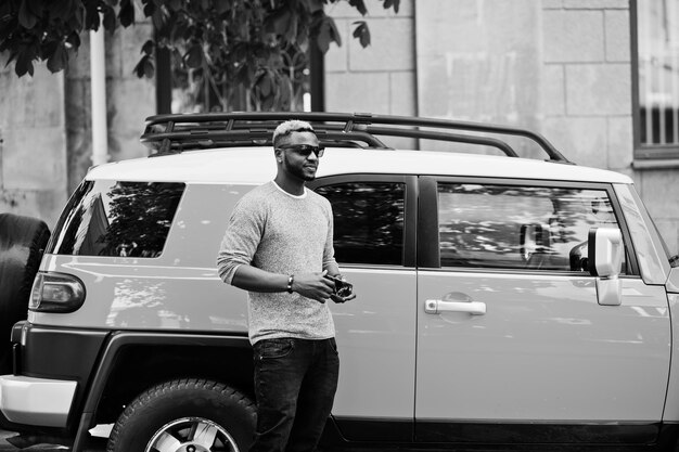 Stylischer afroamerikanischer Junge auf grauem Pullover und schwarzer Sonnenbrille posierte auf der Straße gegen gelbes Auto Modischer schwarzer Geschäftsmann