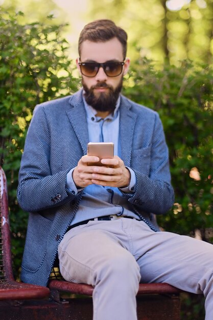 Stylischer bärtiger Mann in blauer Jacke mit Smartphone.