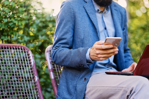 Stylischer bärtiger Mann in blauer Jacke mit Smartphone.