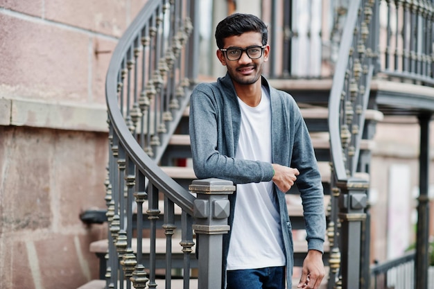 Stylischer indischer Mann mit Brille trägt lässige Posen im Freien gegen Eisentreppen