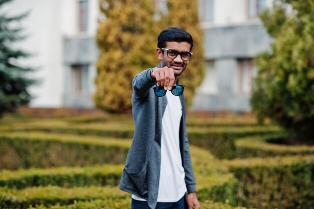 Stylischer indischer Mann mit Sonnenbrille trägt lässige Posen im Freien und zeigt eine doppelte Brille