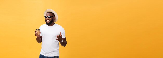 Stylischer junger afrikanisch-amerikanischer Mann, der eine Tasse Kaffee zum Mitnehmen hält, isoliert auf gelbem Hintergrund