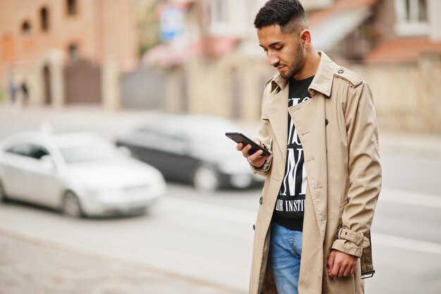 Stylischer kuwaitischer Mann im Trenchcoat-Look auf dem Handy