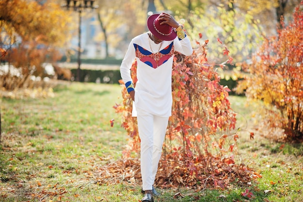 Stylischer, trendiger Afro-Frankreich-Mann mit rotem Hut und weißem Outfit posierte am Herbsttag Schwarzafrikanischer Model-Typ