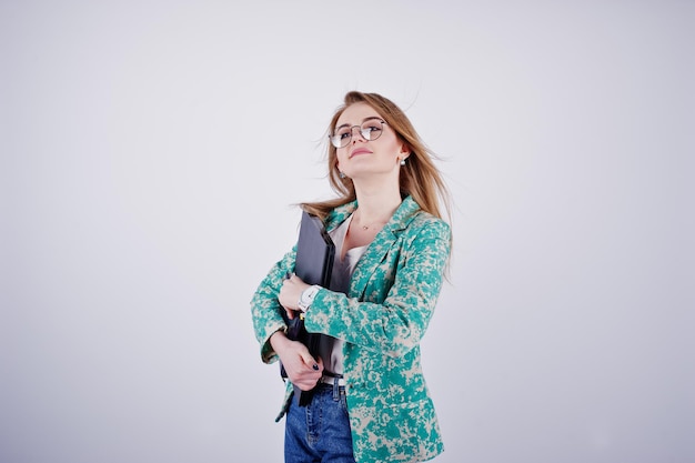 Stylisches blondes Mädchen in Jacke und Jeans mit Brille mit Notizbuch, Tagebuch und Laptop in der Hand vor weißem Hintergrund im Studio