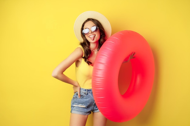 Stylisches Strandmädchen mit Schwimmring, lachend und lächelnd in den Sommerferien, Seereise, glücklich vor gelbem Hintergrund.