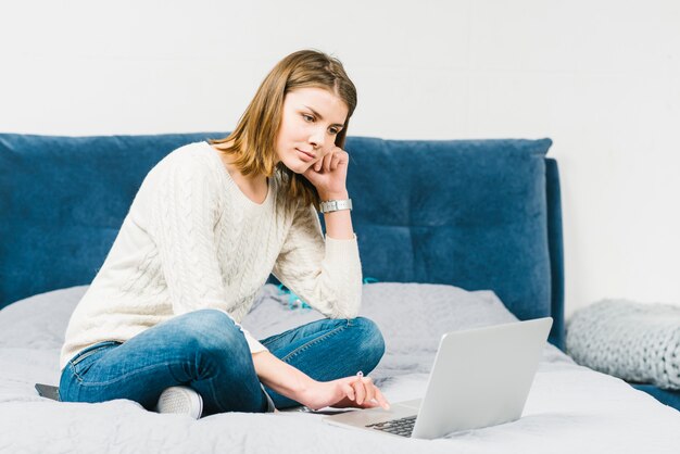 Suchende Laptop der reizenden Frau auf Bett