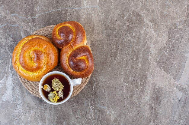 Süße Brötchen und eine Tasse Tee auf einem Untersetzer auf Marmor.