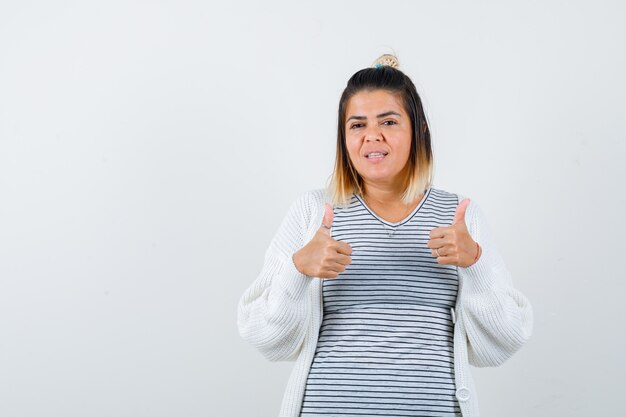 Süße Dame, die doppelte Daumen nach oben in T-Shirt, Strickjacke zeigt und zufrieden aussieht, Vorderansicht.