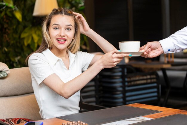 Süße Dame nimmt eine Tasse vom Kellner und lächelt in die Kamera