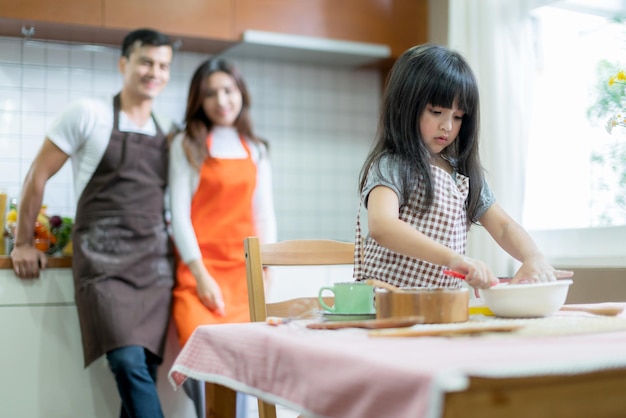 Süße Familien-Wochenendaktivitäten, die zusammen mit Vater, Mutter und Tochter, Glücksmoment und freudigem Hobby-Heimküchenhintergrund kochen