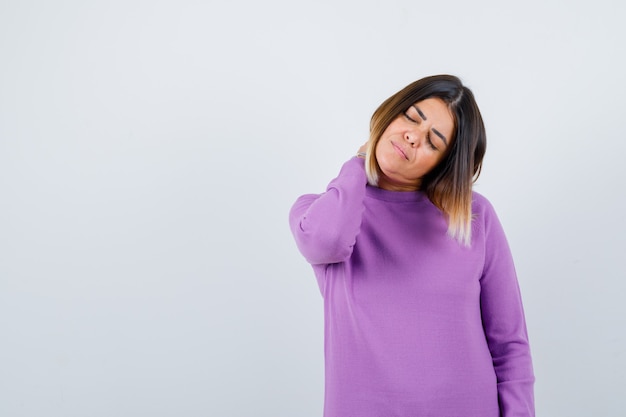 Süße Frau, die Nackenschmerzen in lila Pullover hat und müde aussieht, Vorderansicht.