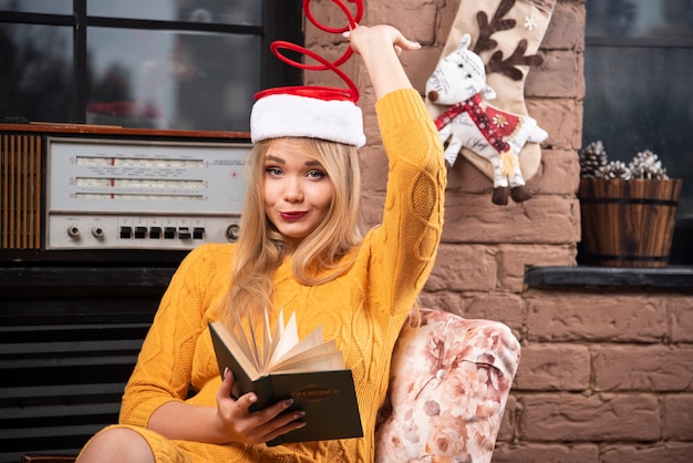 Süße Frau mit Weihnachtsmütze sitzt mit aufgeschlagenem Buch