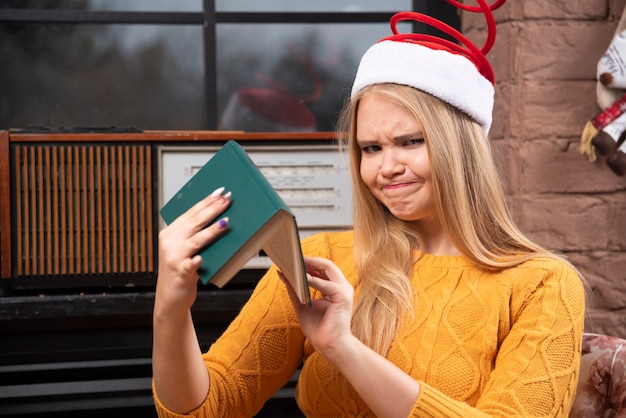 Süße Frau mit Weihnachtsmütze sitzt und liest ein Buch