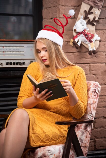 Süße Frau mit Weihnachtsmütze sitzt und liest ein Buch