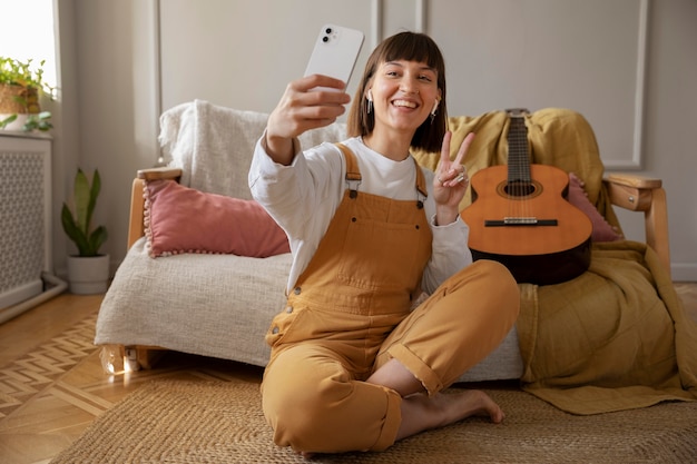 Süße junge Frau, die neben ihrer Gitarre ein Selfie macht