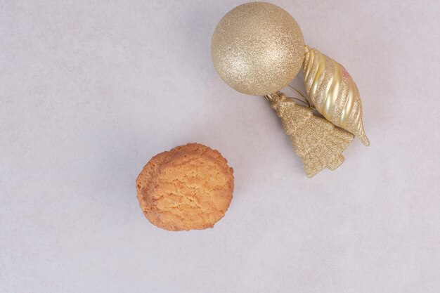 Süße Kekse mit goldenen Weihnachtsspielzeugen auf weißer Oberfläche
