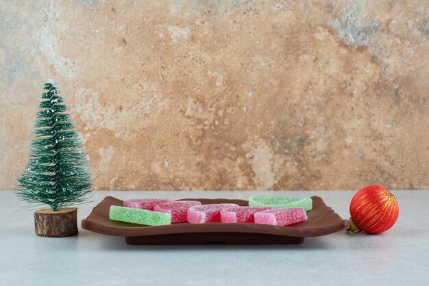Süße Marmelade mit Weihnachtskugel und Baum auf dunklem Teller.