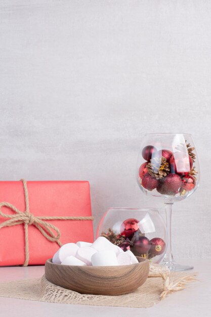 Süße Marshmallows auf Holzteller mit Glas roter Weihnachtskugeln