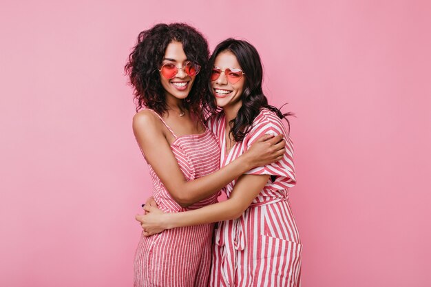 Süße romantische Mädchen umarmen sich freundlich. Damen in rosa Sonnenbrille lachen.