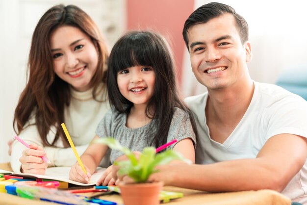 Süße schwarze Haare Kind weibliche Tochter Hausaufgaben und Lachen zusammen mit Eltern im Wohnzimmer Hauskonzept