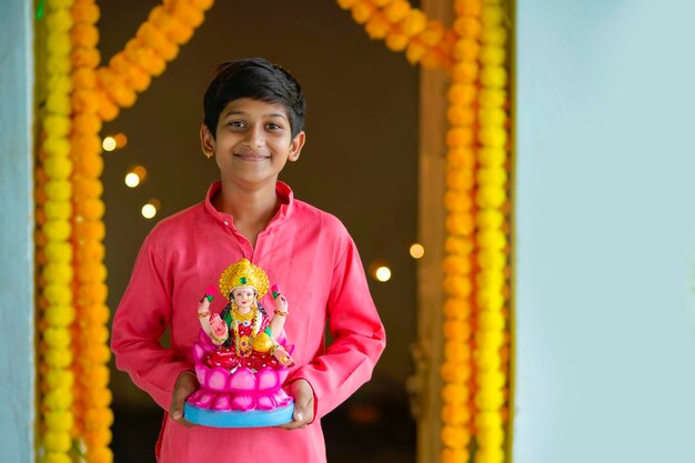 Süßer indischer kleiner junge, der die göttin laxmi in der hand hält und das diwali-festival feiert.