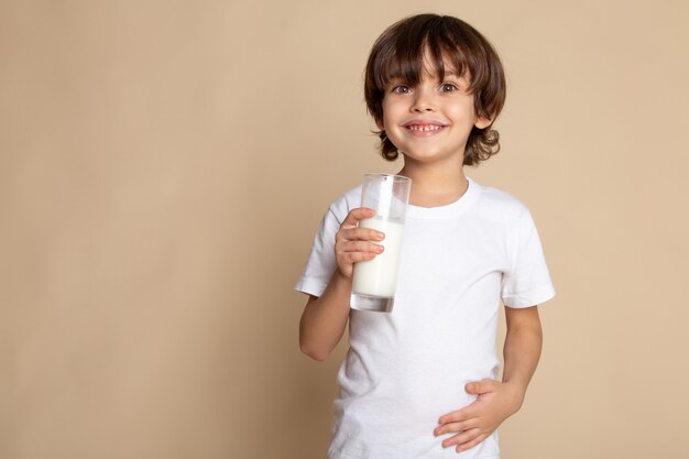 süßer Junge entzückend im weißen T-Shirt, das weiße Vollmilch auf rosa Schreibtisch trinkt