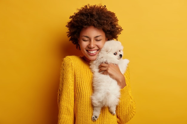 Süßer Schuss der fröhlichen Afro-Frau umarmt mit großer Liebe ihren Spitzhund