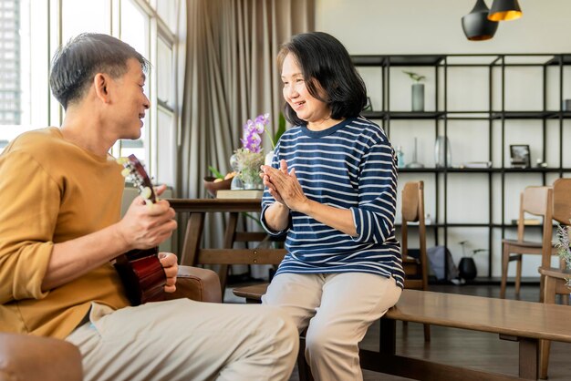 Süßes asiatisches Seniorenpaar singt, spielt akustisches Ukulele-Instrument Glückliches Lächeln Ältere Großeltern, die Spaß haben und ihr Leben im Ruhestand genießen Lifestyle-Party glücklicher Lebensstil