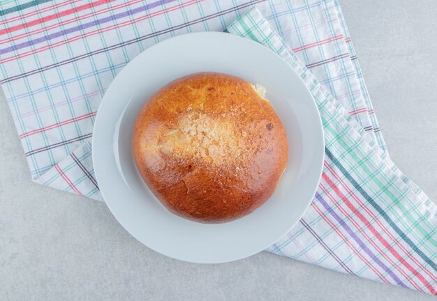 Süßes Brötchen mit Stoff auf weißem Teller.