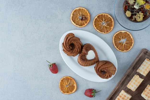 Süßes Gebäck mit getrockneter Orange und Tasse Kräutertee auf Marmorhintergrund. Hochwertiges Foto