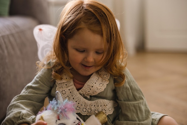 Süßes, hellhäutiges kleines rothaariges Mädchen im Kleid spielt am Wochenende zu Hause mit Spielzeug Kindheitskonzept