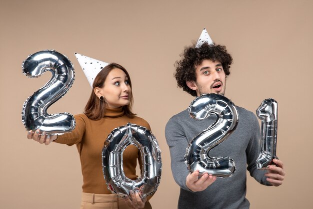 Süßes junges Paar tragen Neujahrshut posiert für Kamera Mädchen zeigt und und Kerl mit und auf Grau