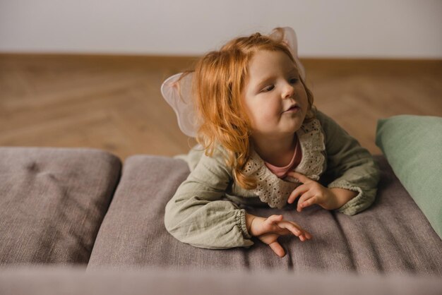 Süßes kleines kaukasisches Mädchen mit roten Haaren liegt morgens auf dem Sofa Kindheitskonzept