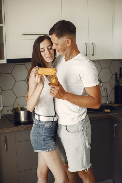 Süßes Paar in einer Küche. Dame in einem weißen T-Shirt. Paar zu Hause essen gekochten Mais.