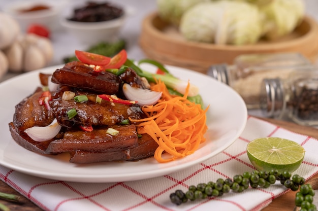 Süßes Schweinefleisch in einem weißen Teller mit gehackten Frühlingszwiebeln, Chili, Limette, Kürbis, Tomate und Knoblauch.