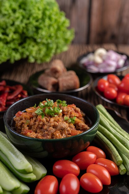 Süßes Schweinefleisch in einer schwarzen Schüssel mit Gurken, langen Bohnen, Tomaten und Beilagen