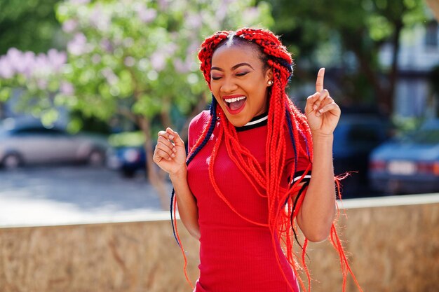 Süßes und schlankes afrikanisch-amerikanisches Mädchen in rotem Kleid mit Dreadlocks in Bewegung, das sich auf der Straße amüsiert Stilvolles schwarzes Modell