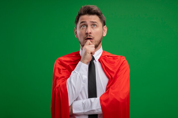 Superheld-Geschäftsmann im roten Umhang, der verwirrt über grüner Wand steht