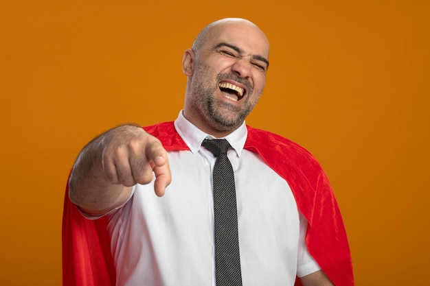 Kostenloses Foto superheld geschäftsmann im roten umhang zeigt auf sie lachend über orange wand stehend