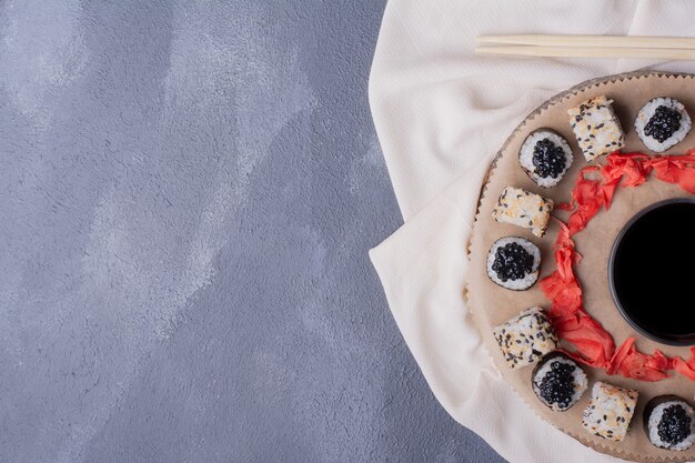 Sushi-Set. Maki und Alaska Sushi Rolls auf Holzteller mit Tischdecke, eingelegtem Ingwer und Sojasauce.