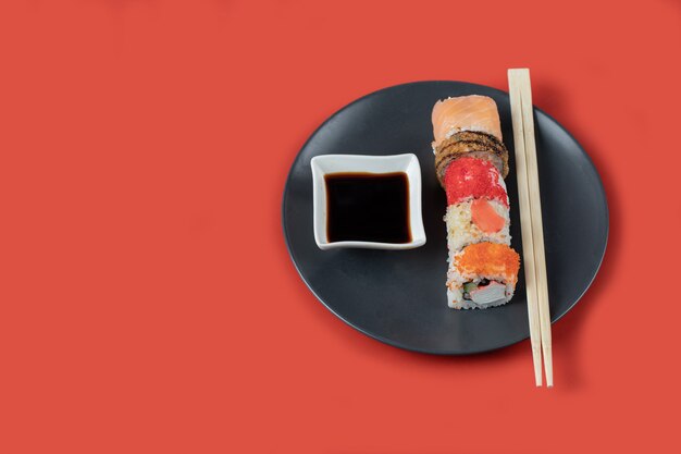 Sushi-Set mit Saucen in einer schwarzen Platte auf rotem Tisch.